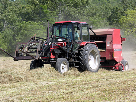 Hay baler sweeping up the wind rows of dried grass